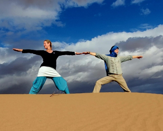 Die beiden Kursleiterinnen machen Yoga-Übungen auf einer Sanddüne.